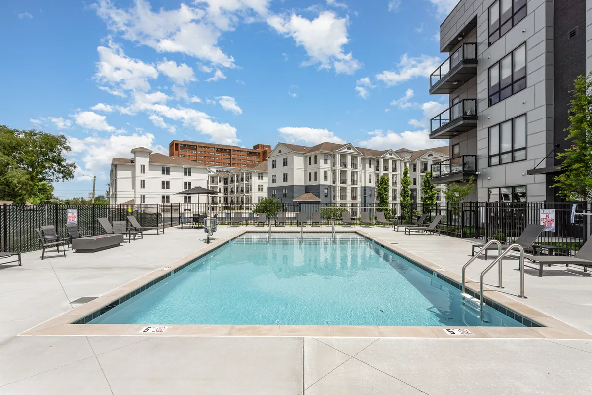 This poolside exterior image displays a sparkling swimming pool bordered by lounge chairs and city buildings in the distance. The relaxed, inviting setting signals comfort and the promise of downtime after days spent exploring Nashville.