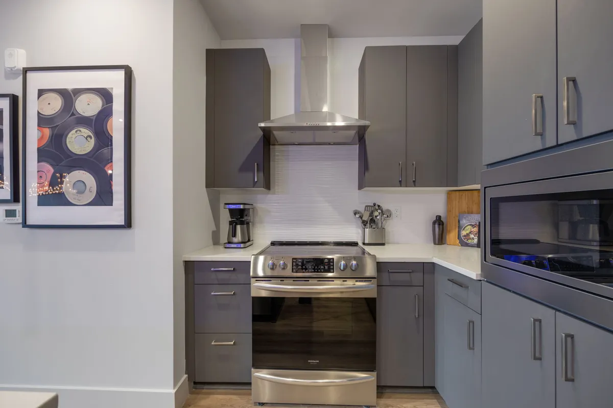 A close-up of the stainless steel stove, kitchen cabinets, a coffee maker, and framed artwork. The setup is practical and cozy, focusing on the key culinary features mentioned in the section.