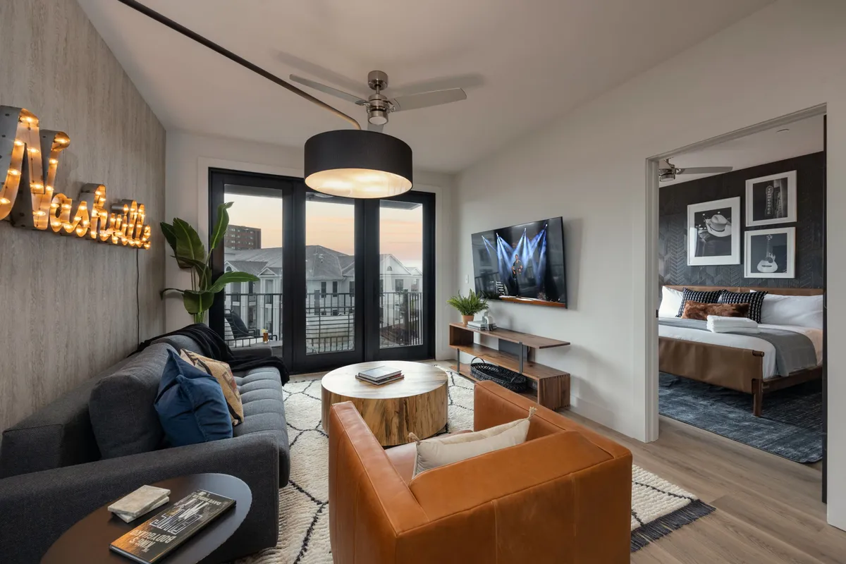 A chic living area featuring a brown leather chair, wooden coffee table, and oversized windows. The 'Nashville' sign adds a stylish local touch. The windows highlight the brightness of the room and the potential for city views.