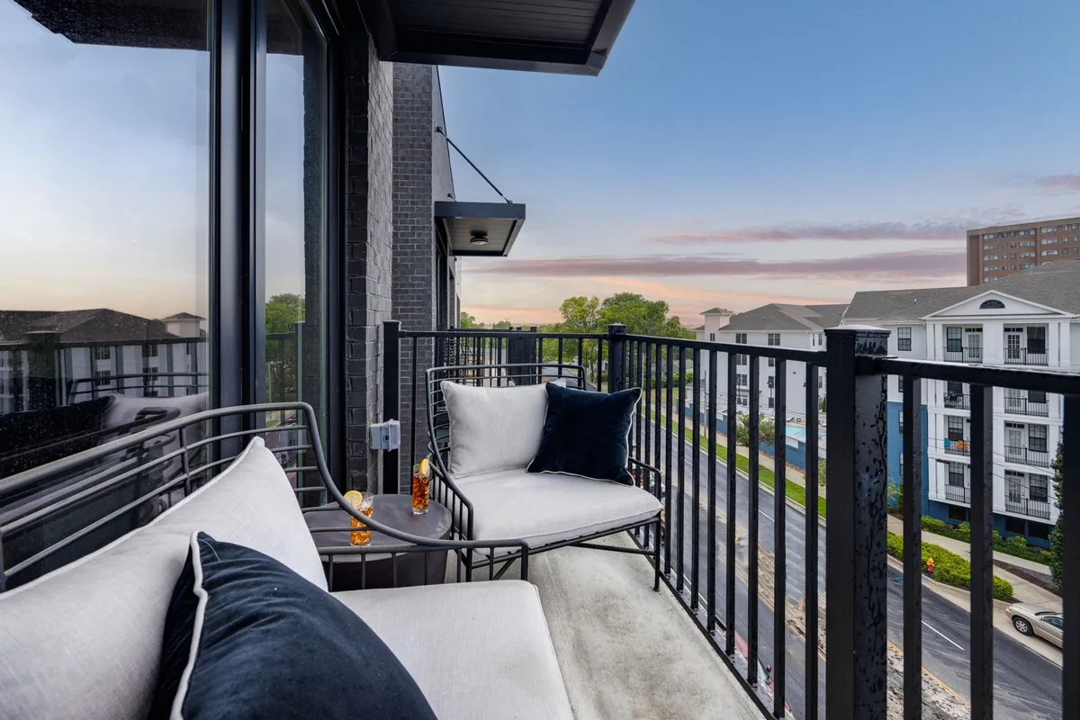 An inviting balcony space with comfortable seating and decorative cushions, overlooking the street and city buildings. The space is perfect for relaxing, enjoying the sunset, or unwinding with friends while taking in city skyline views.